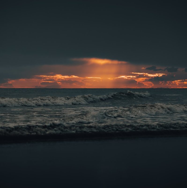 the sun is setting over the ocean on a cloudy day